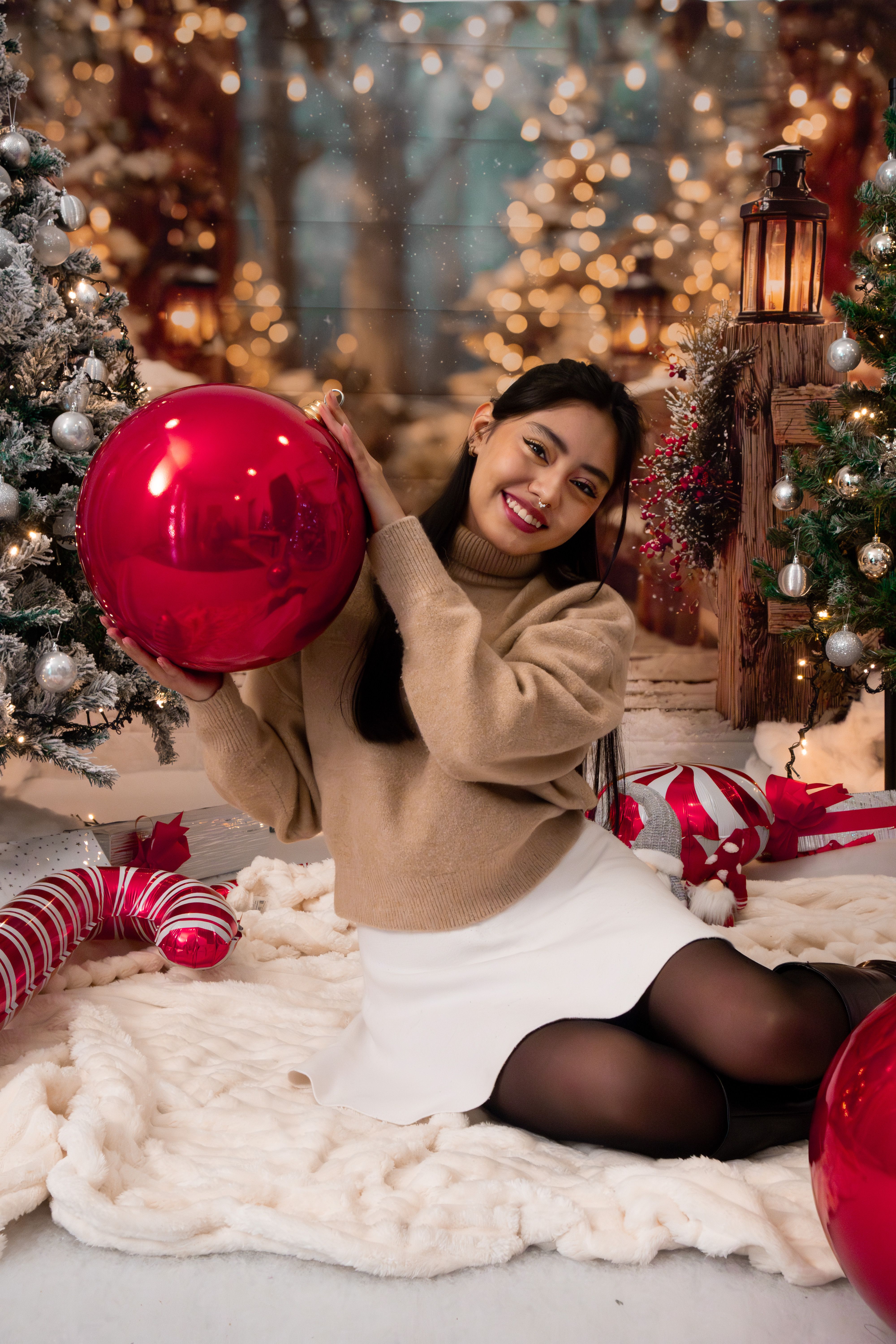 Fotomural Mujer sonriente sosteniendo un adorno rojo en un acogedor entorno navideño con luces.