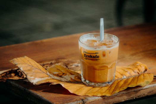 Creamy iced coffee on a wooden table with vibrant autumn leaves, capturing a cozy fall vibe.