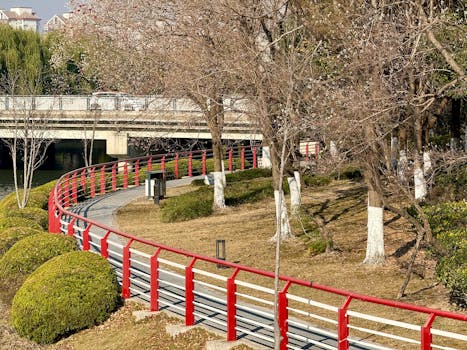 Una luminosa giornata di sole a Shanghai con un sentiero nel parco caratterizzato da suggestive ringhiere rosse e alberi spogli.
