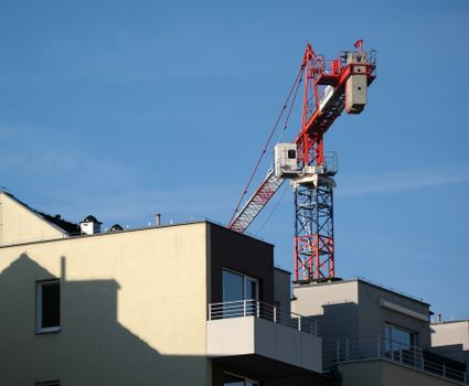 A red construction crane towering over a modern building against a clear blue sky.