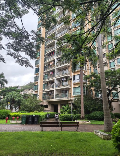 Free High-rise apartment building surrounded by lush trees and a well-maintained park area. Stock Photo