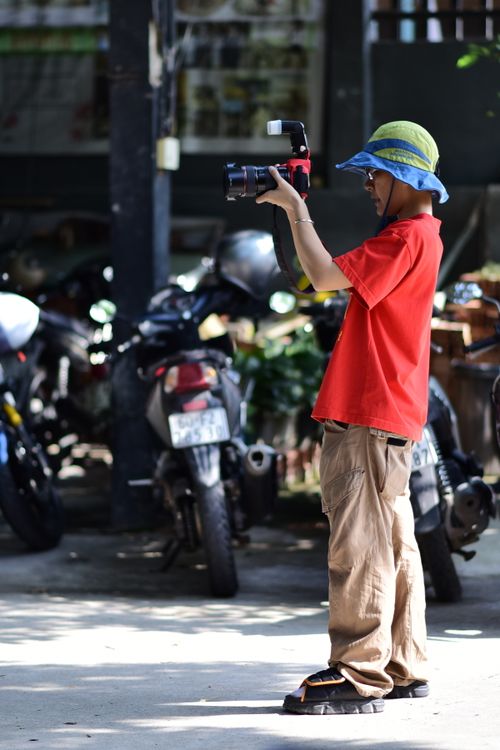 Free A young photographer in a red shirt and blue hat takes pictures outdoors with a DSLR camera. Stock Photo