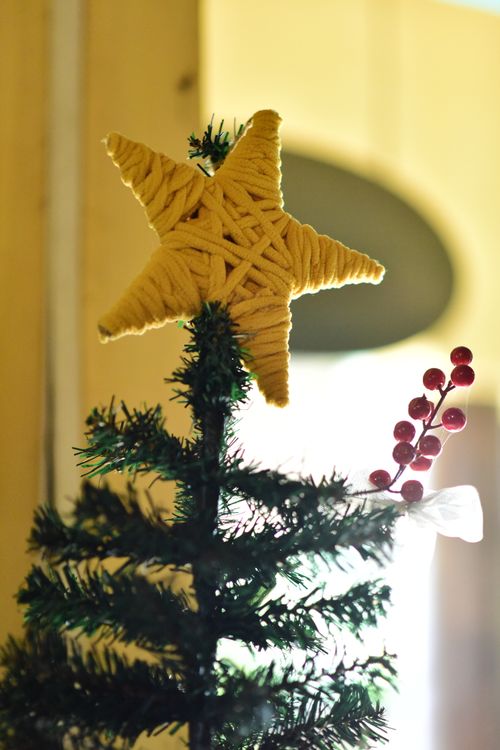 Free Close-up of a Christmas tree with a yarn star topper indoors capturing holiday spirit. Stock Photo