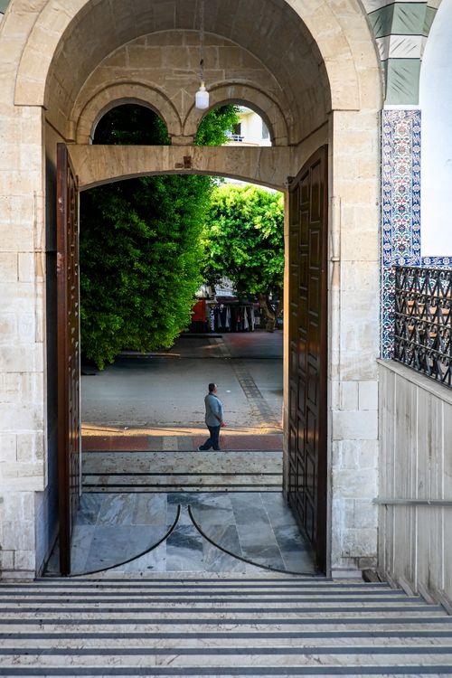 Free Man walking down a tree-lined street viewed through a grand stone archway. Stock Photo