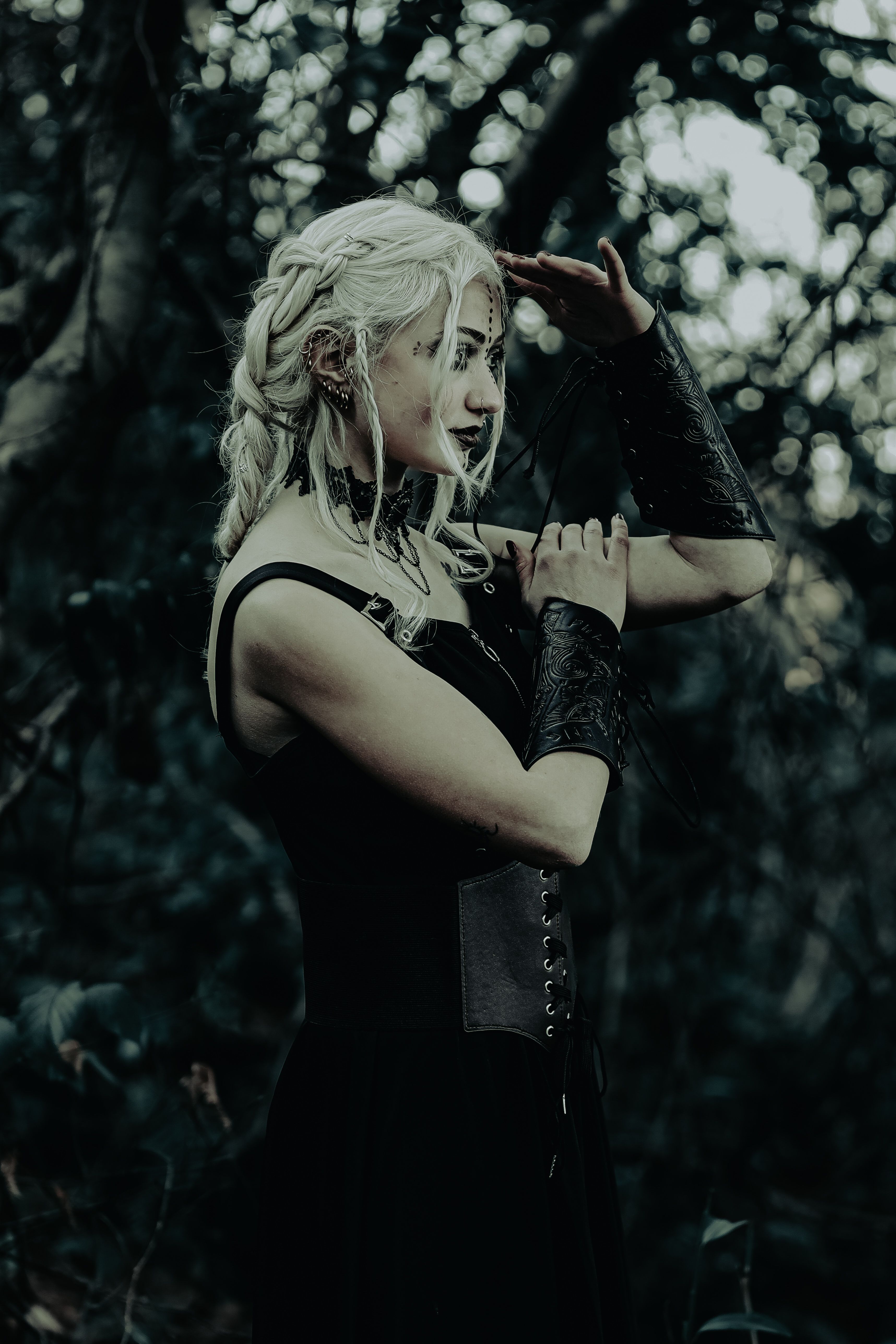 Side profile of a warrior woman with braided hair and leather bracers gazing into the distance in a dark forest