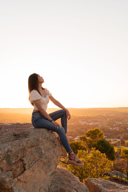 白襯衫和藍色牛仔牛仔褲，坐在岩石上的女人