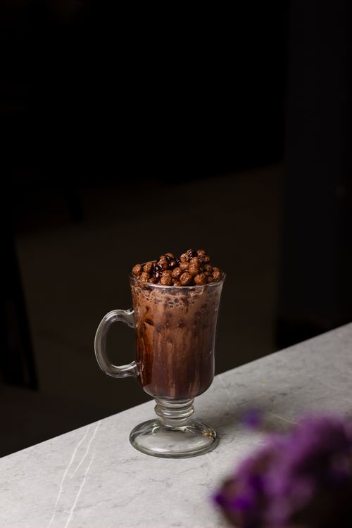 Free A delicious glass of hot chocolate topped with crunchy cocoa balls on a marble table. Stock Photo