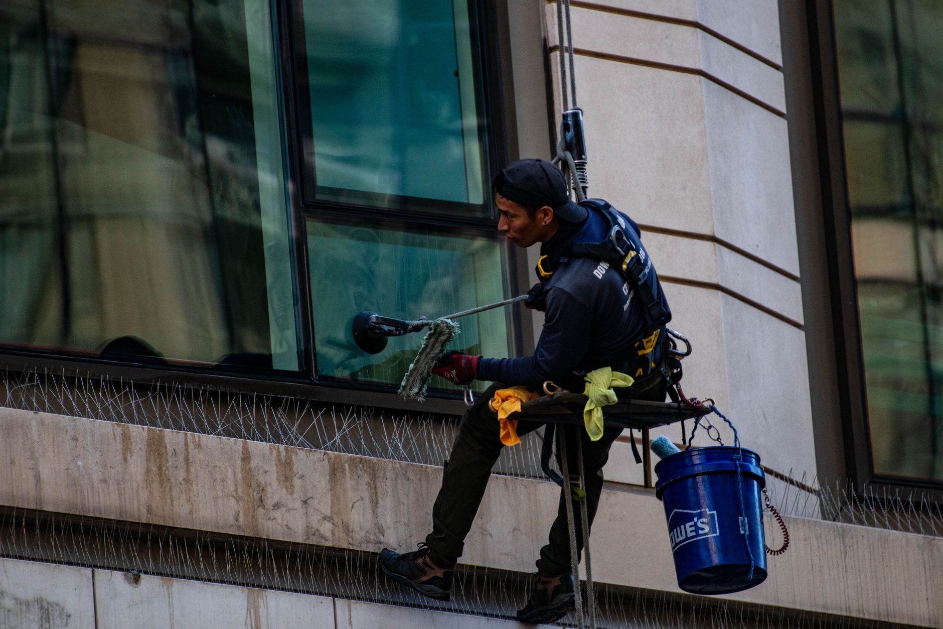 Window cleaner on a safety harness working a multi-story building exterior.