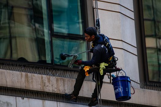 Man cleaning high-rise building windows using safety harness outdoors in daylight.
