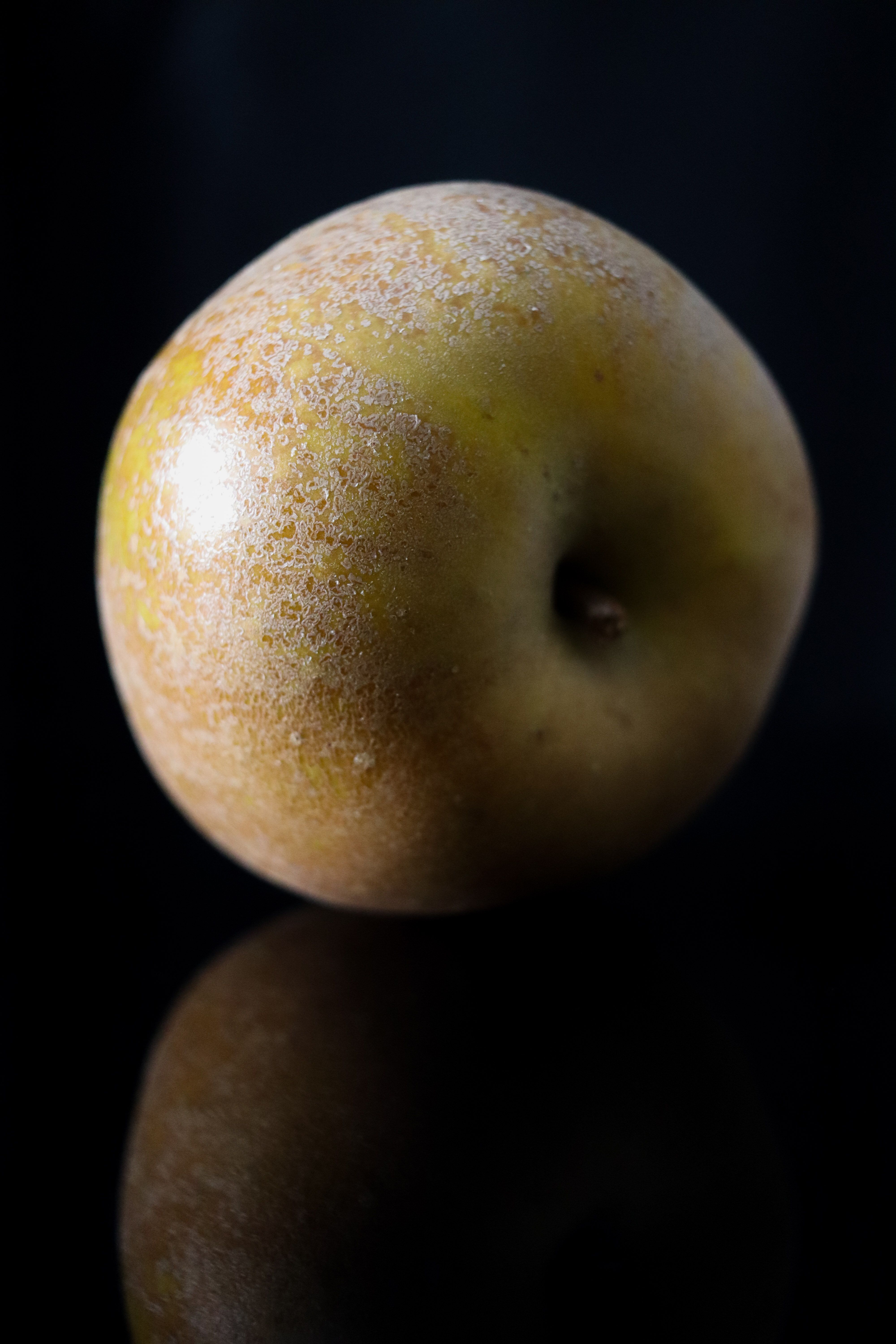 Close-up of a golden apple on a black reflective surface, highlighting its texture.