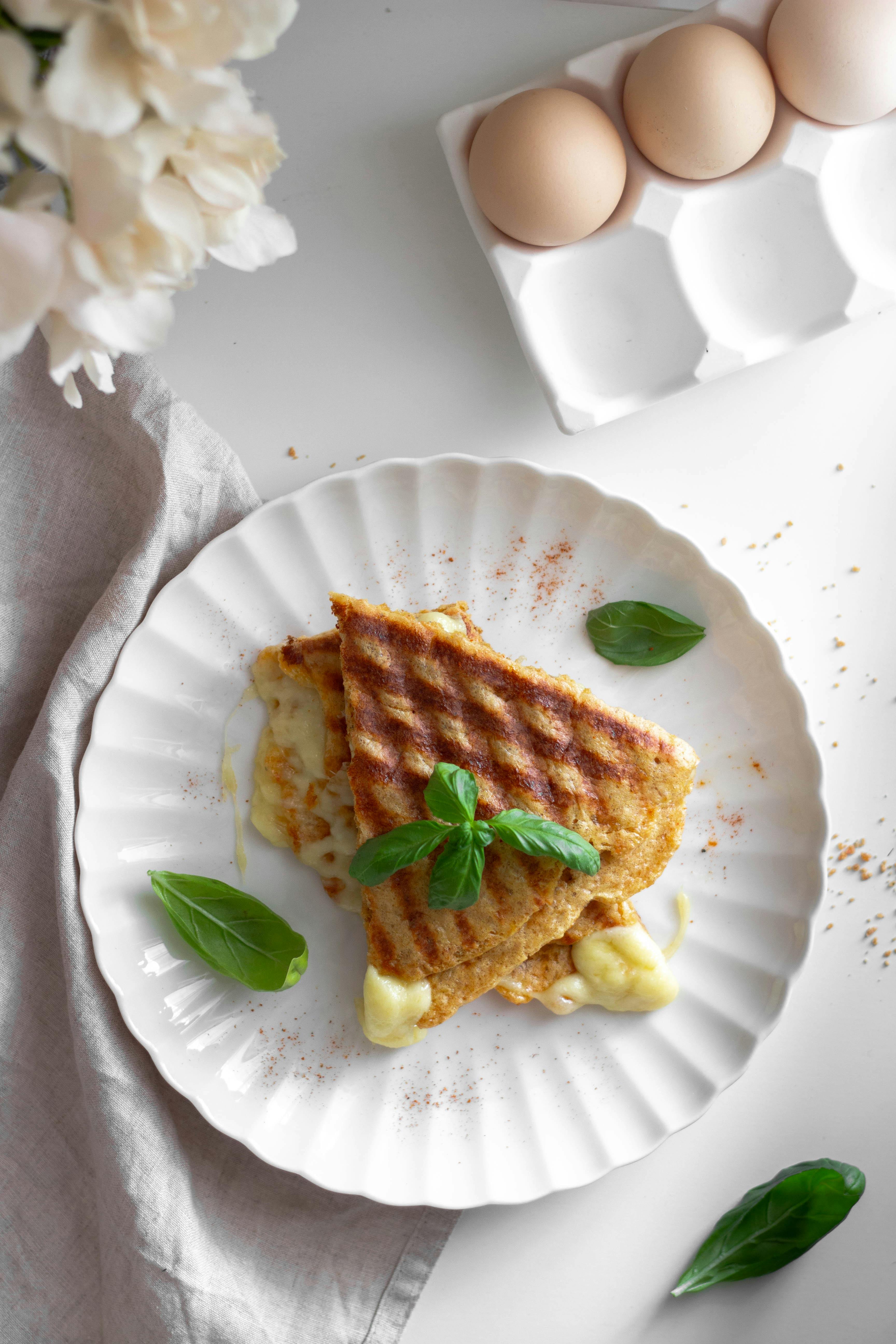 Tasty grilled cheese sandwich on white plate, garnished with fresh basil.