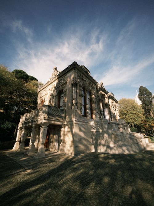 Free Elegant historic stone villa surrounded by lush trees and a blue sky backdrop. Stock Photo