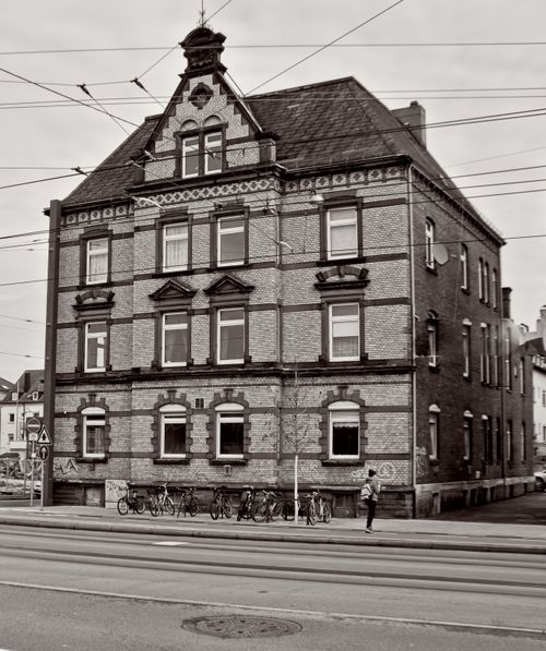 Free A monochrome image featuring an old brick building with ornate details and a person standing nearby. Stock Photo