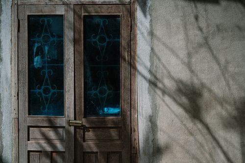 Free A rustic wooden door with artistic glass panels, sunlit with shadows cast on adjacent wall. Stock Photo