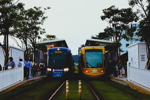 Colorful trams at a station in Taipei, bustling with commuters and surrounded by trees.