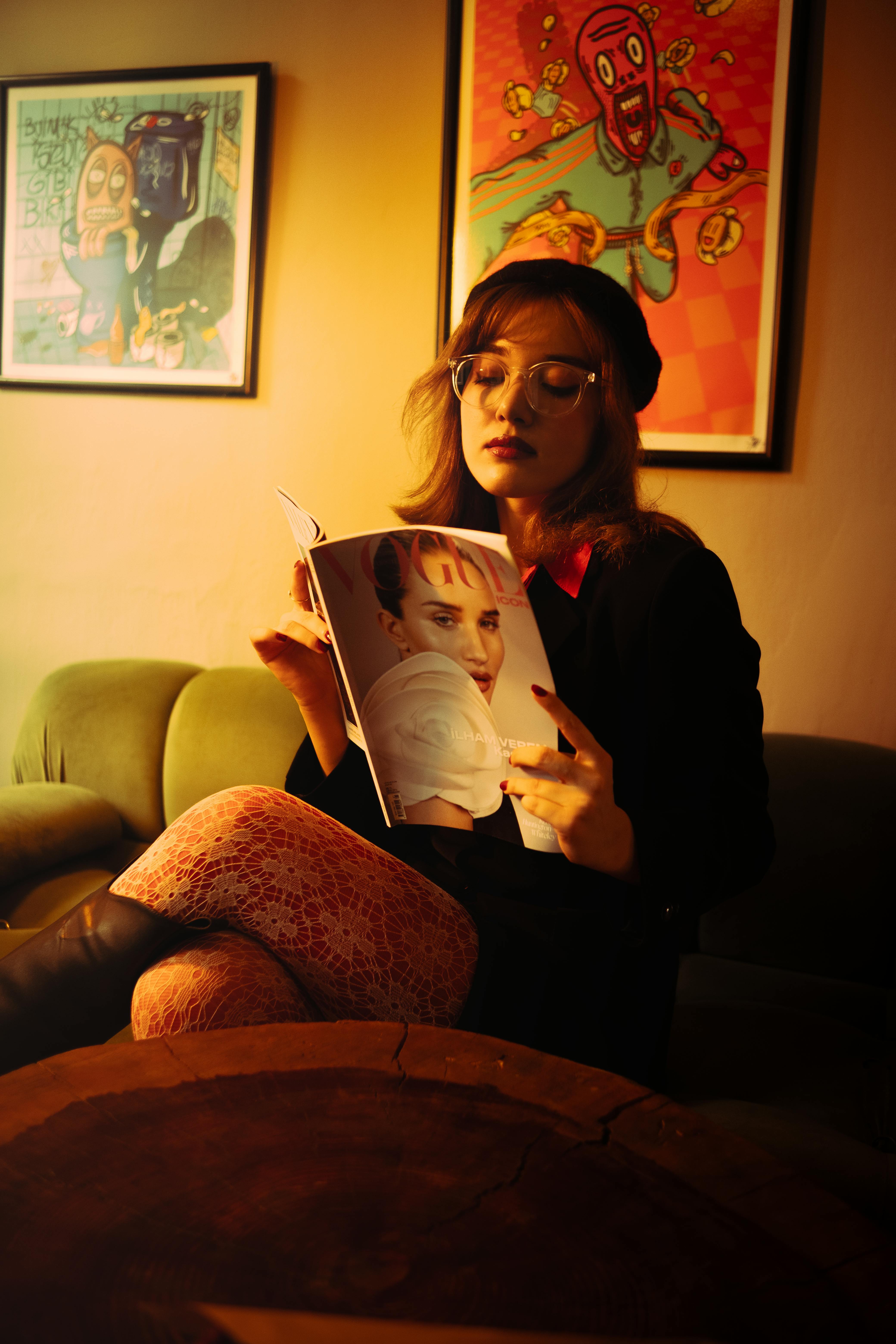 Free A young woman reads a magazine in a cozy, dimly lit café in İzmir, Türkiye, surrounded by art. Stock Photo