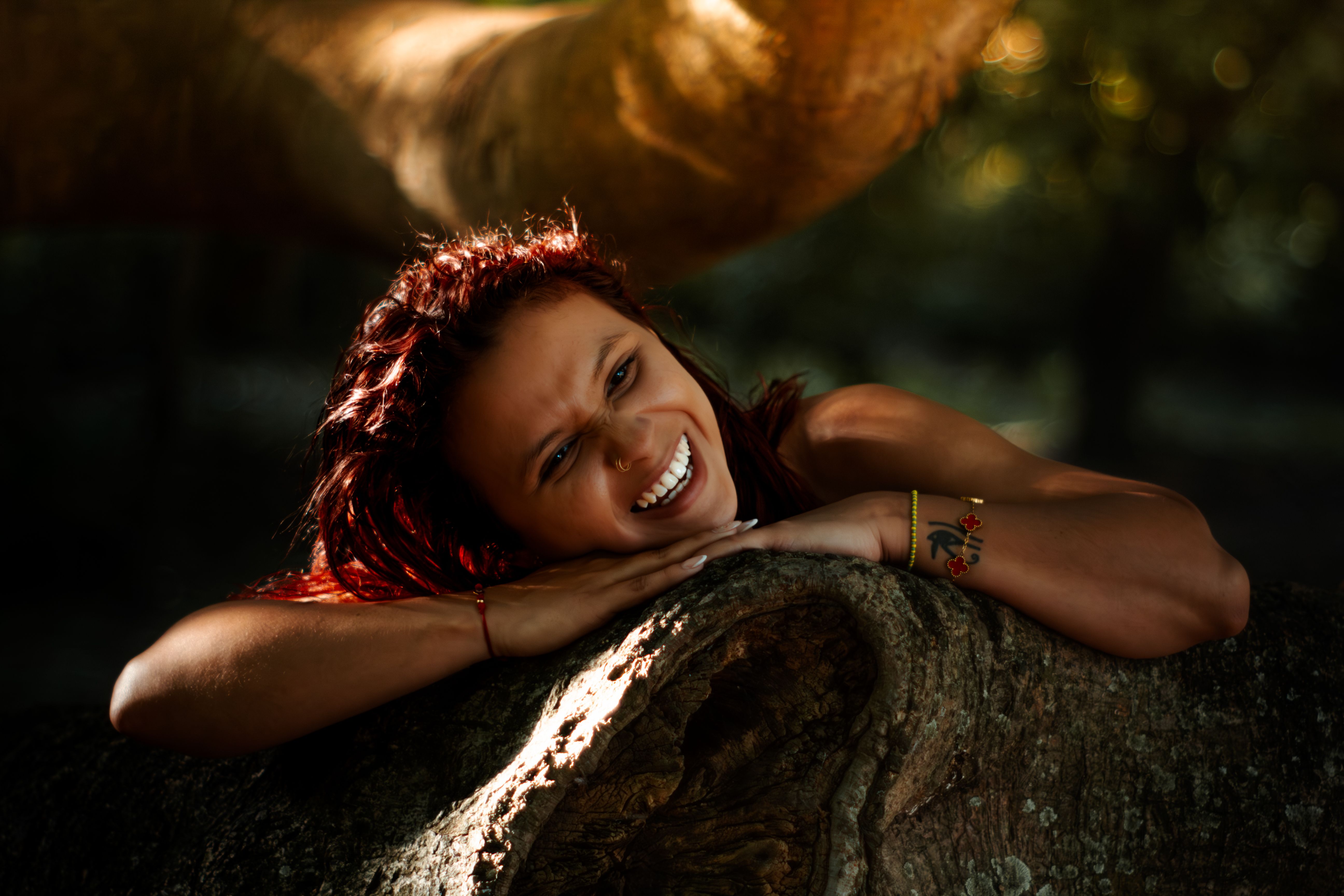 Happy woman with red hair laughing while relaxing outdoors on a tree trunk.