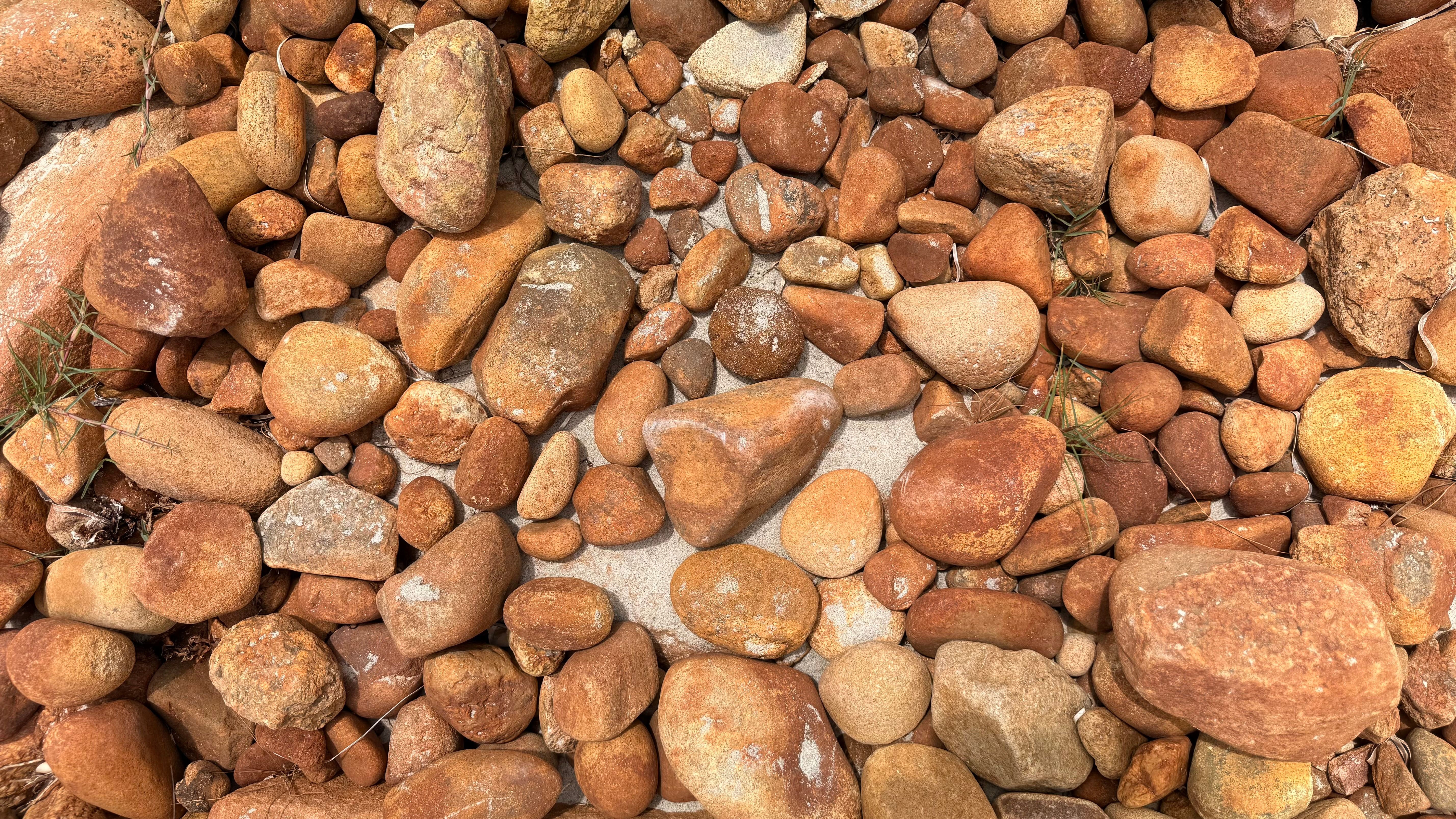 Top view of various brown stones on a sandy surface with natural texture.