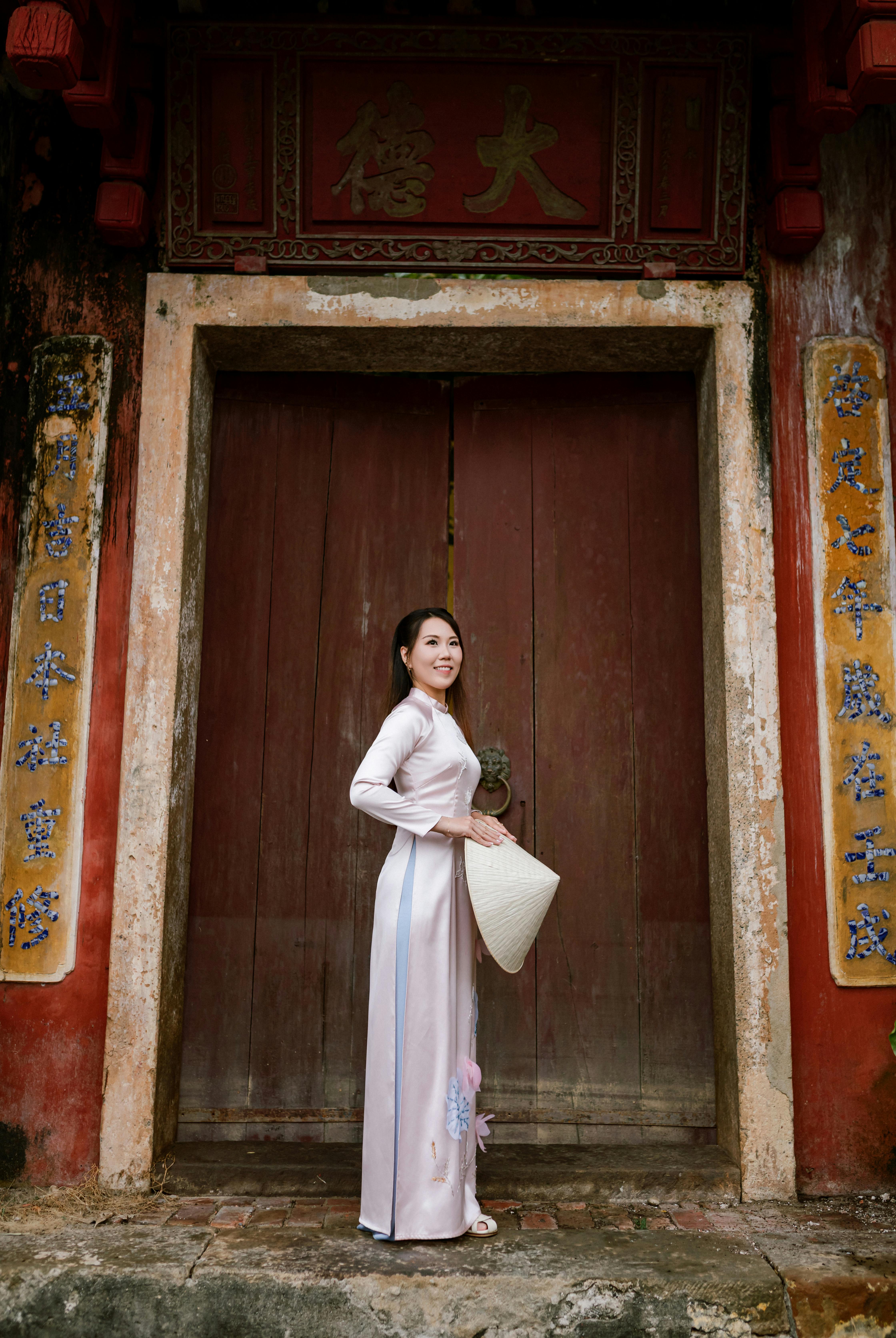 A woman in an ao dai poses gracefully in front of an ancient door in Hội An, Vietnam.