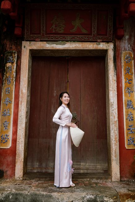 A woman in an ao dai poses gracefully in front of an ancient door in Hội An, Vietnam.