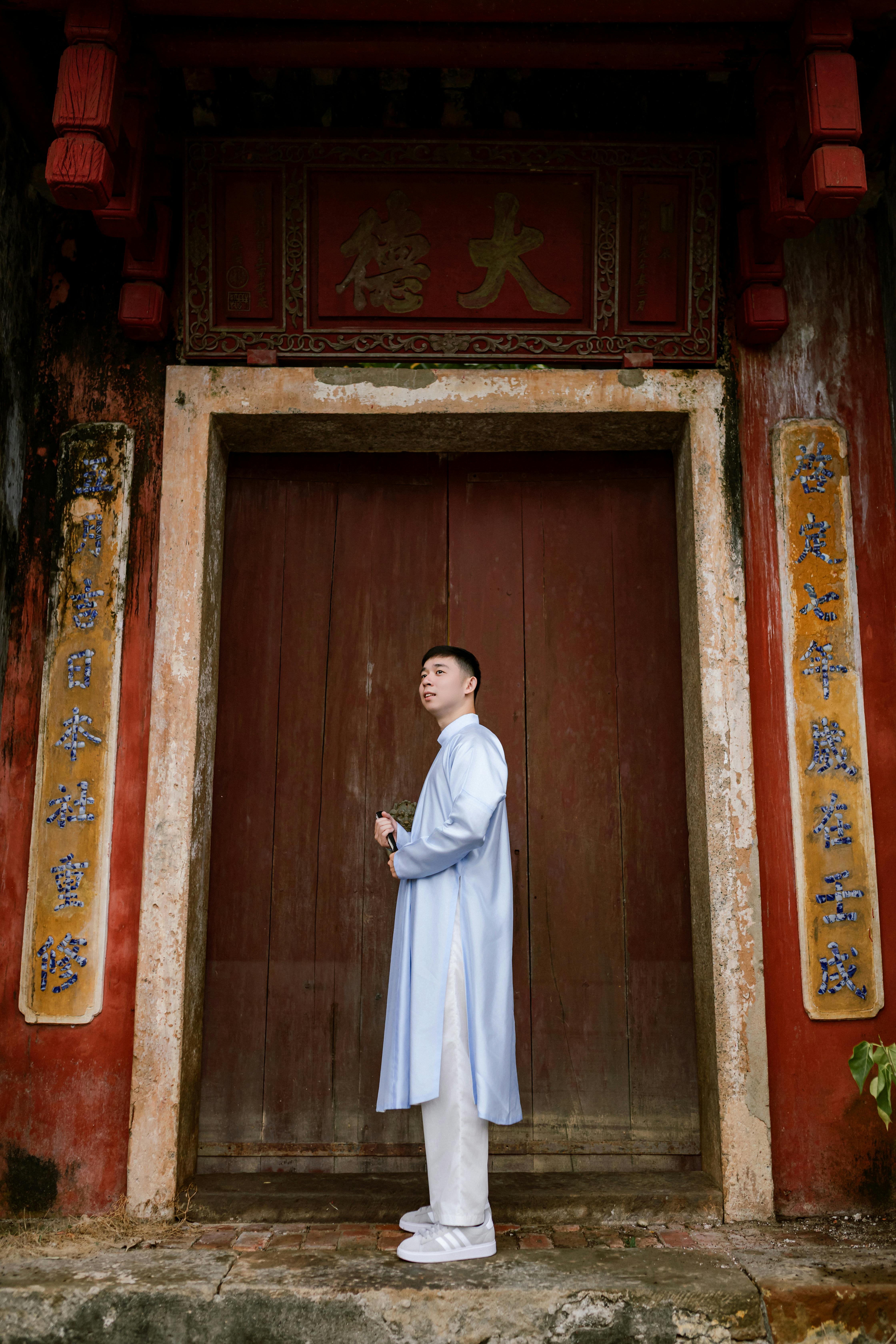 Man in traditional Vietnamese clothing standing before ancient Hoi An building.