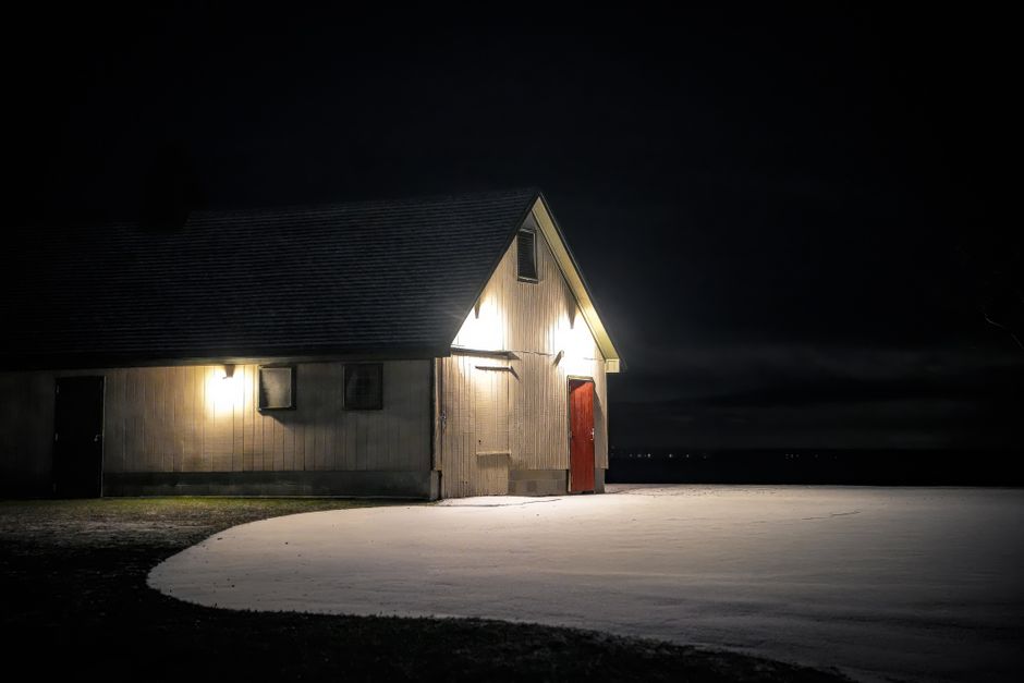 A warmly lit cabin stands alone on a snowy night, offering a peaceful winter scene.