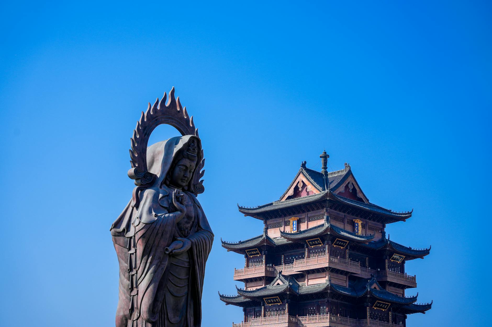 Majestic Buddha statue and traditional Asian pagoda under a clear blue sky.