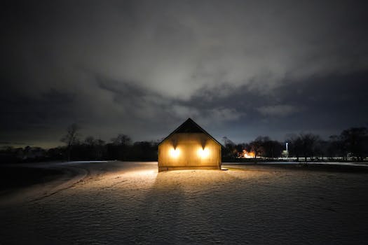 Illuminated barn at night with dramatic sky and snowy field.