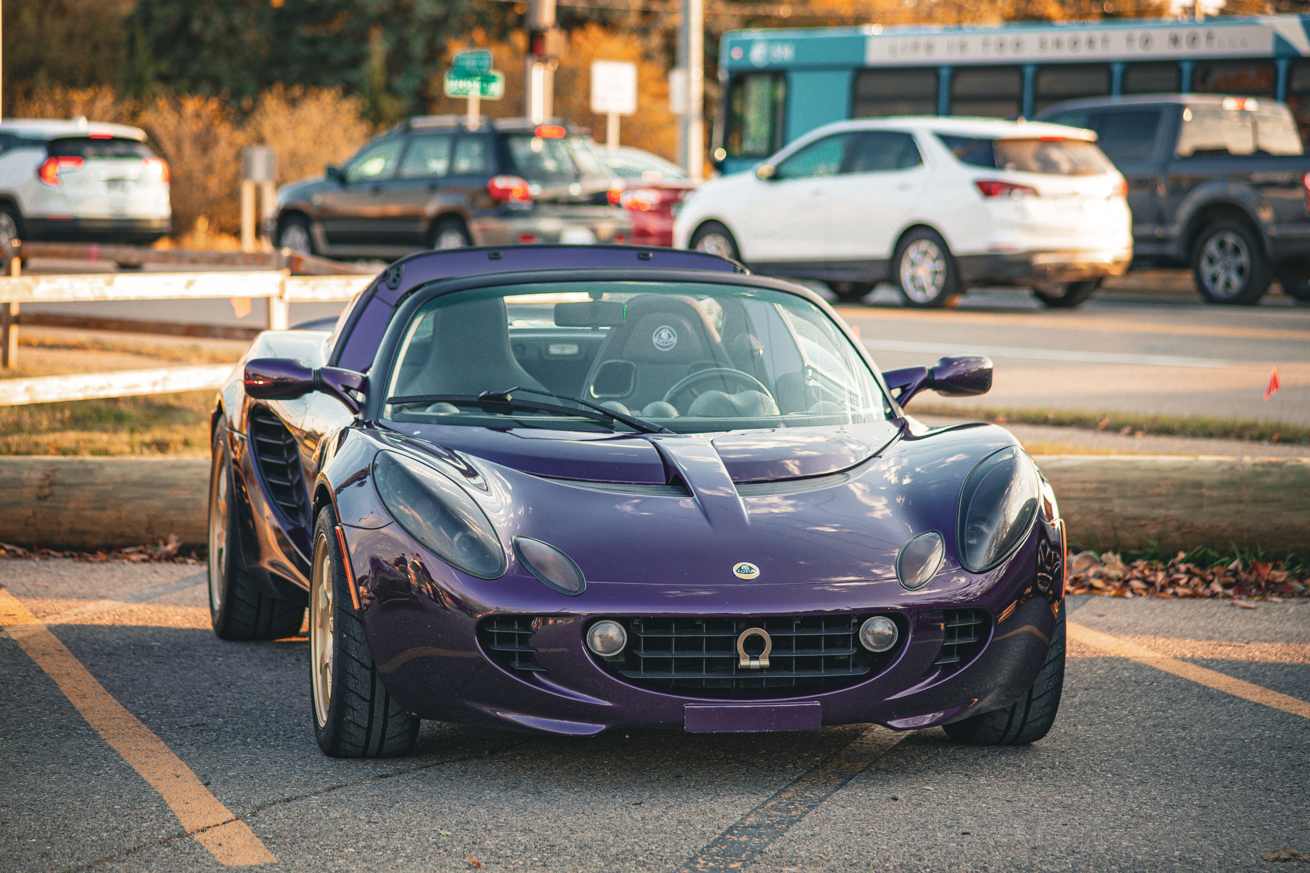 Vibrant purple sports car parked outdoors; daylight scene with autumn backdrop.