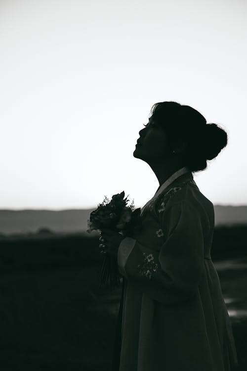 Женщина в сером платье с длинными рукавами держит букет цветов