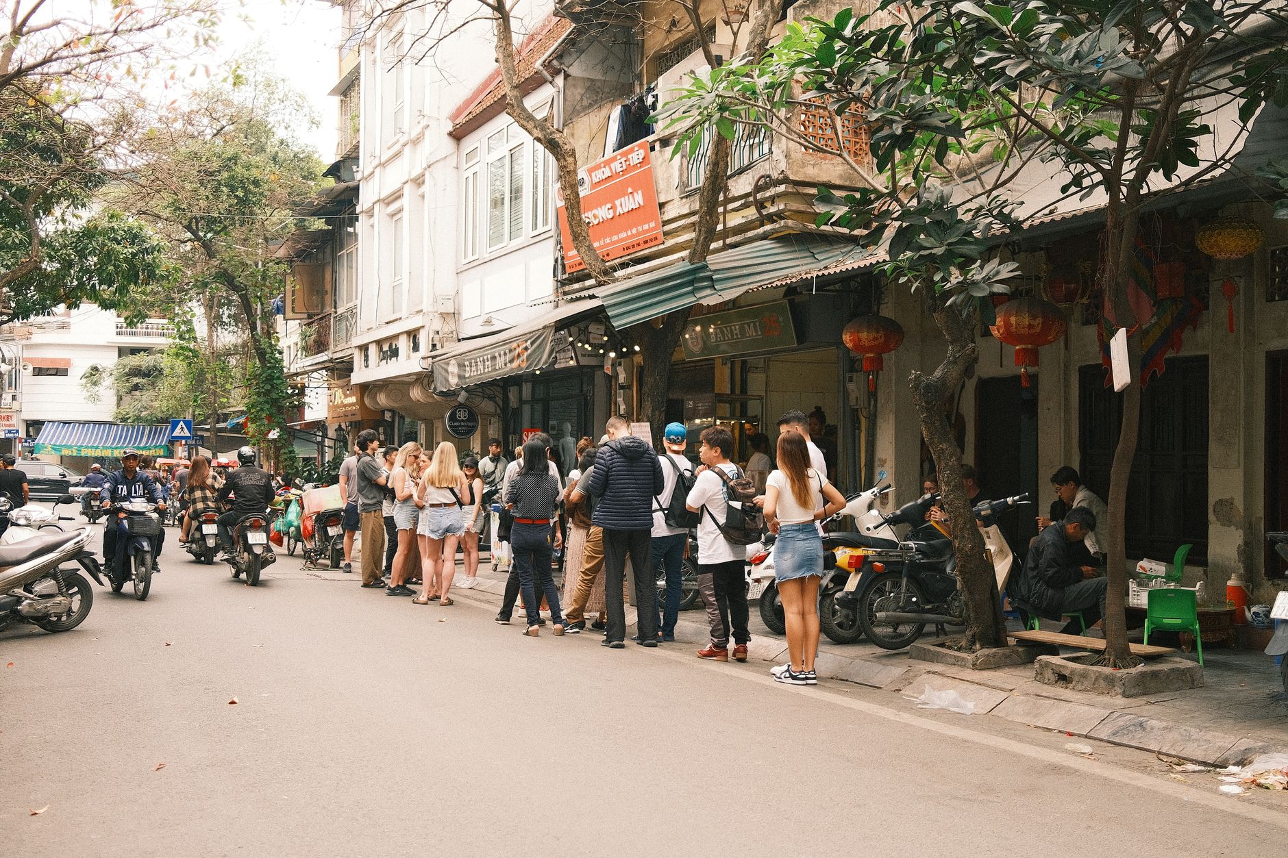Bustling street scene in Hanoi featuring people lined up outside a shop, capturing the lively atmosphere.