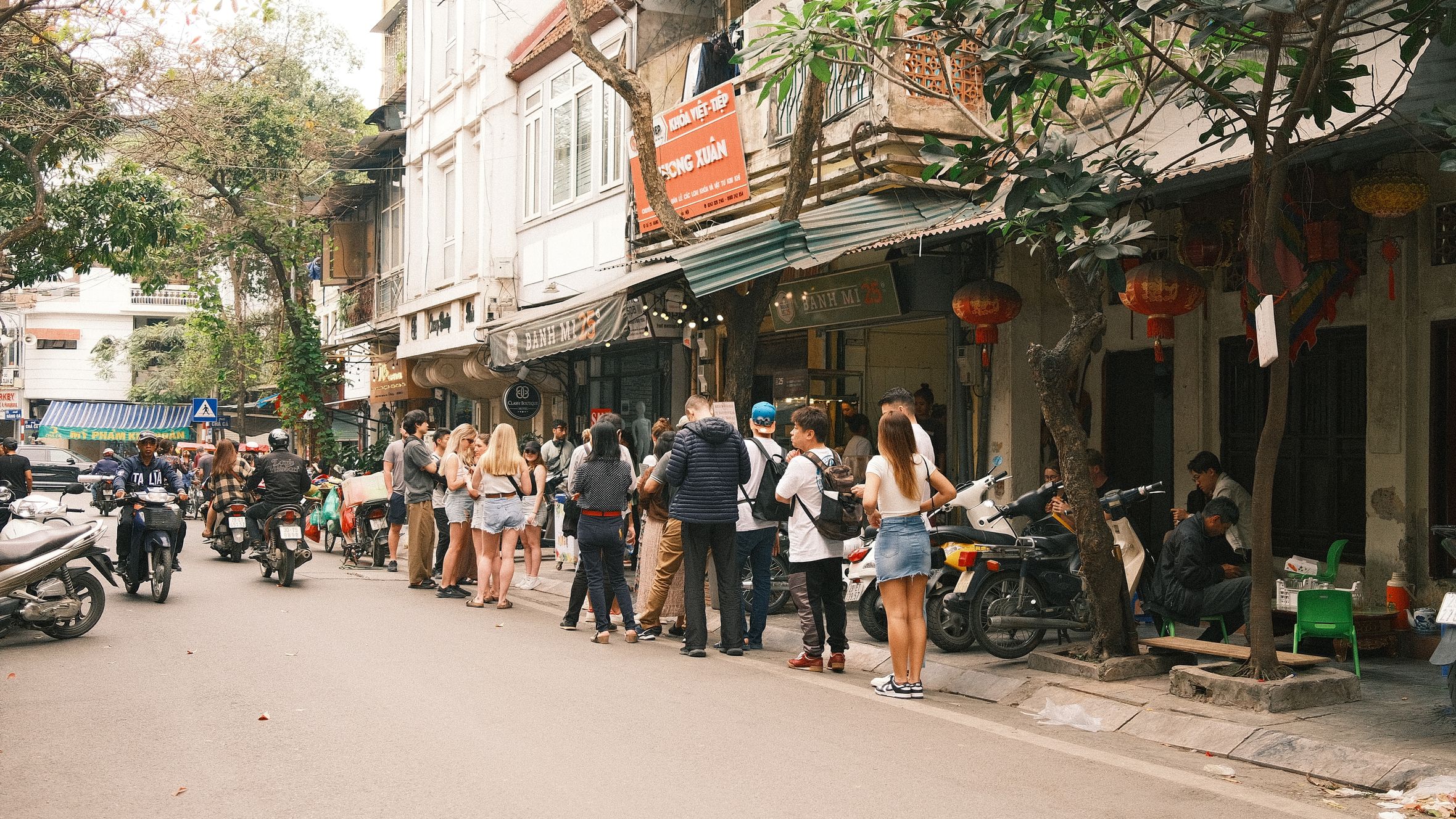 Bustling street scene in Hanoi featuring people lined up outside a shop, capturing the lively atmosphere.