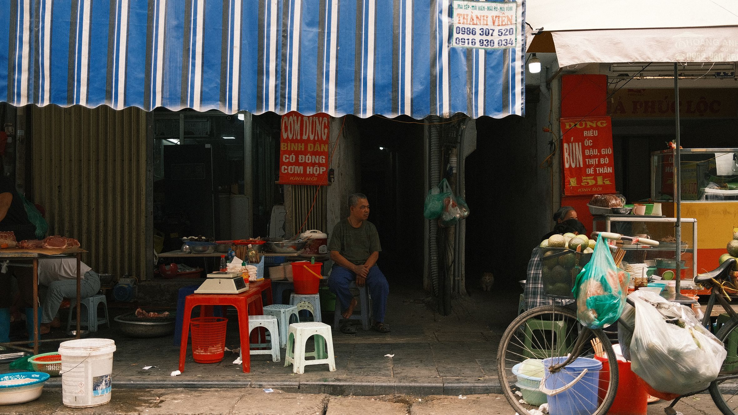 Lively street market featuring food vendors, awnings, and a parked bicycle.