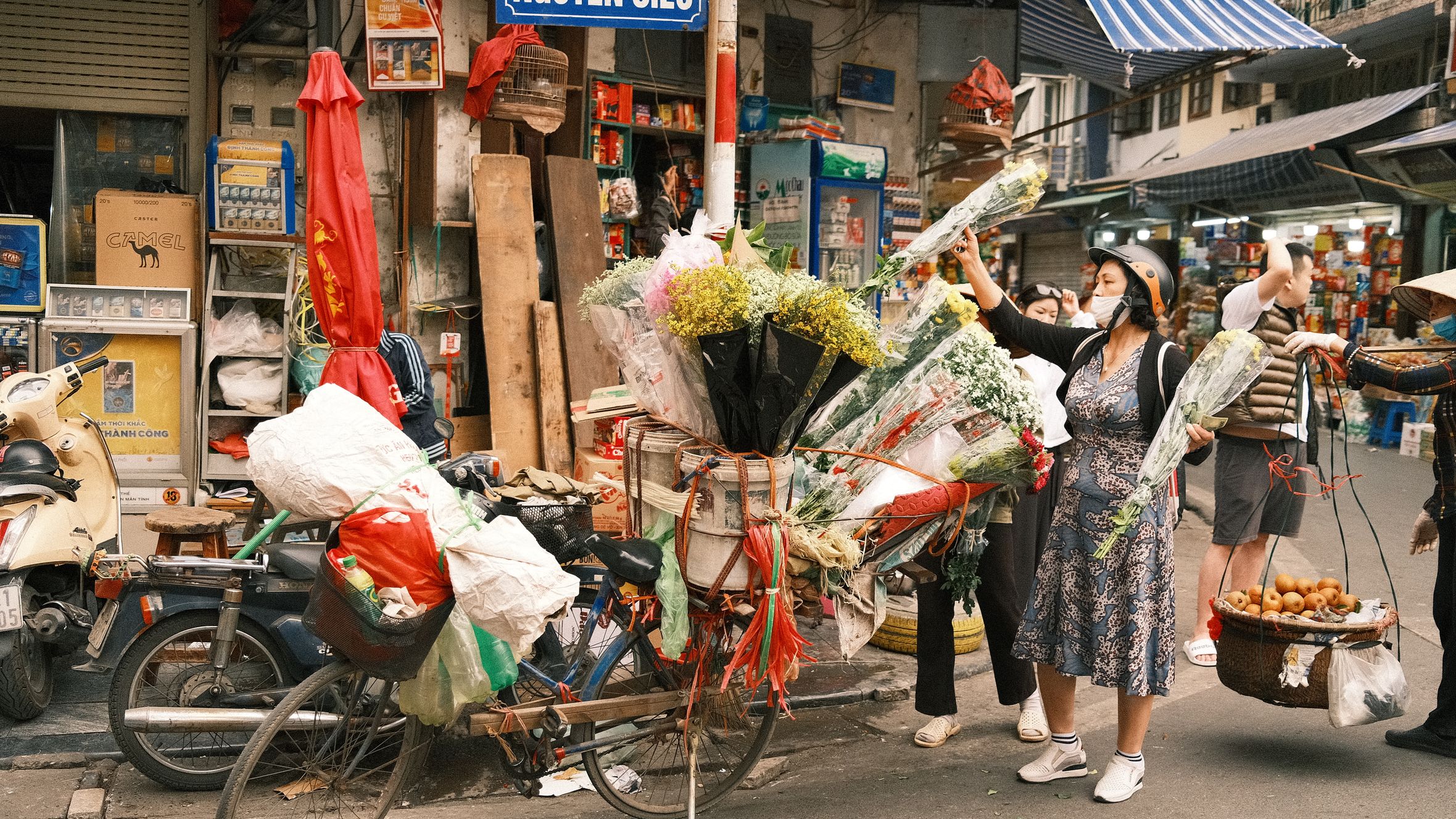 A bustling street in Hanoi with a woman buying flowers from a bicycle vendor.
