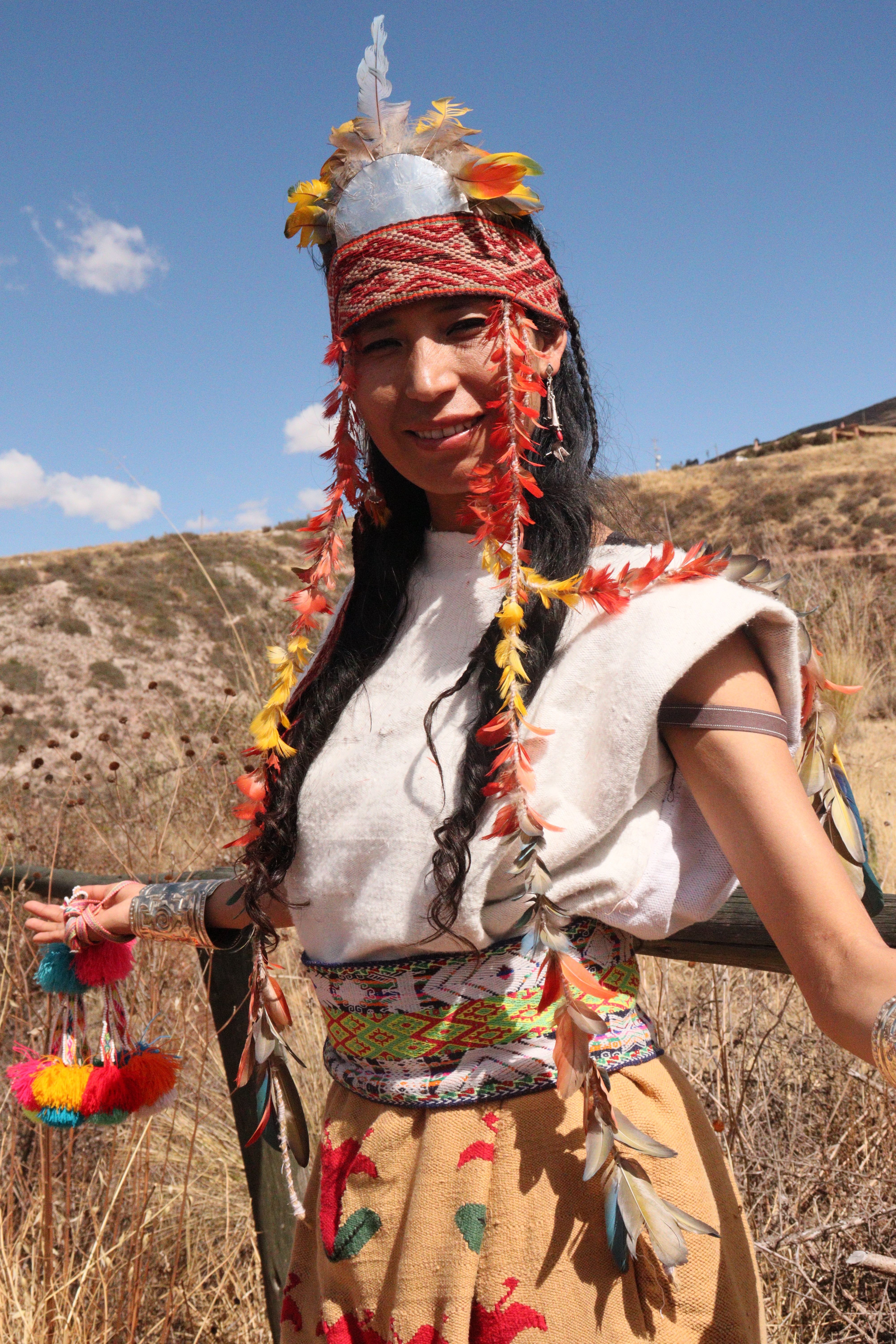 Woman in traditional attire smiling outdoors under clear sky.