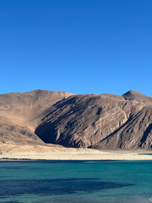 Free Stunning view of a mountain range against a clear blue sky with a serene lake in the foreground. Stock Photo