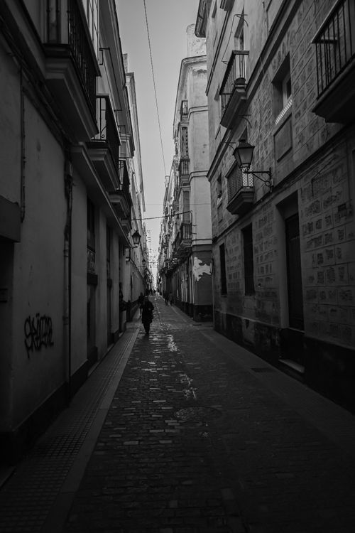 Free Black and white photo of a narrow urban street with a single person walking, creating a moody atmosphere. Stock Photo