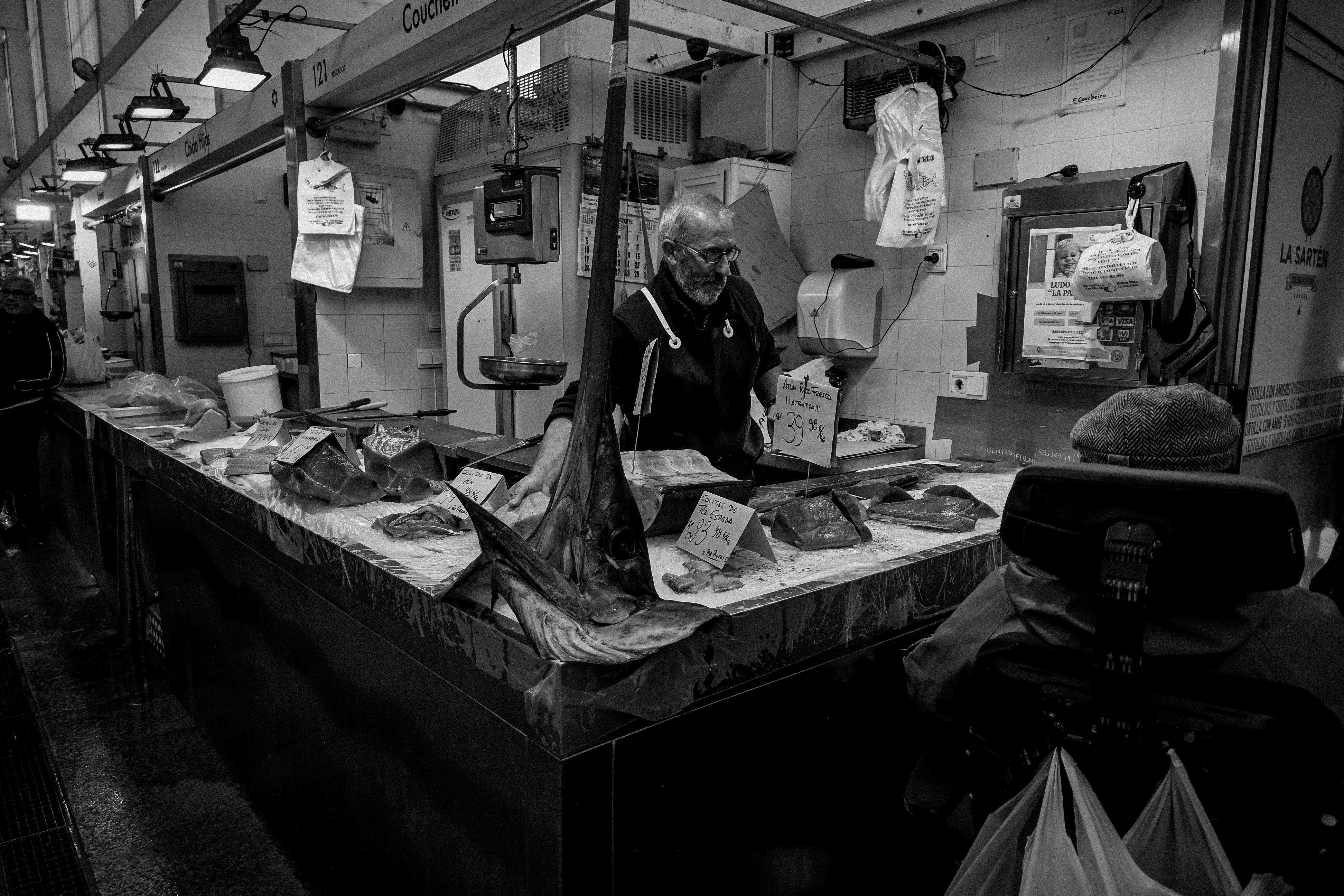 Monochrome image of a fish stall interaction at a market with a seller and a customer.