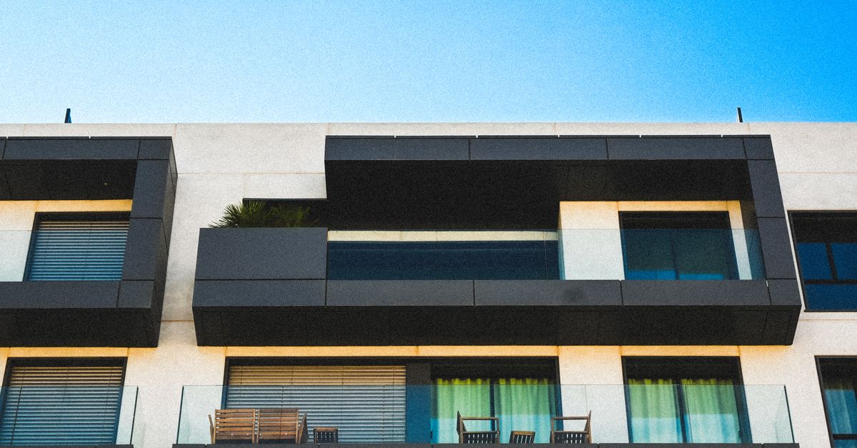 Minimalist apartment facade with glass balconies against a clear blue sky.