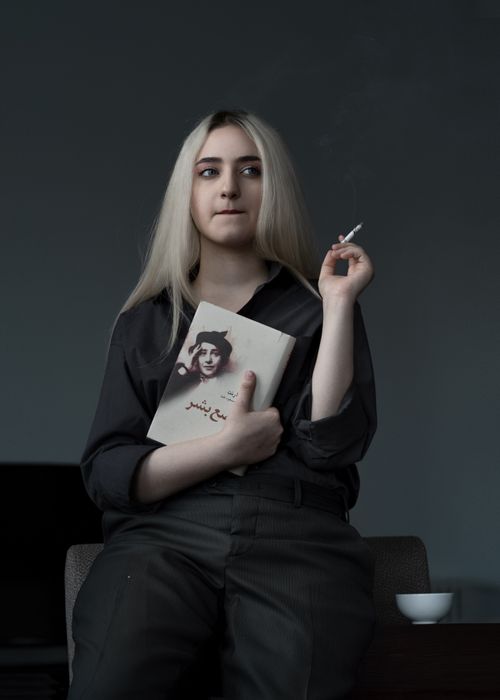 Free Pensive woman holding a book and cigarette, sitting indoors with a contemplative expression. Stock Photo