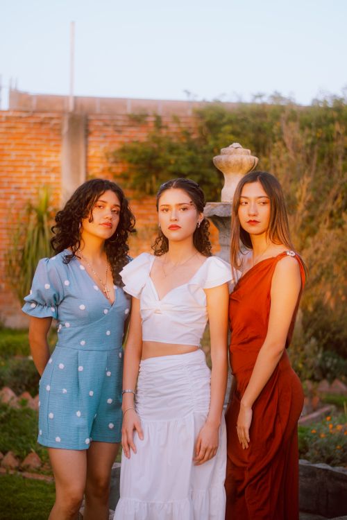 Free Three stylish young women posing confidently in elegant dresses outdoors during daytime. Stock Photo