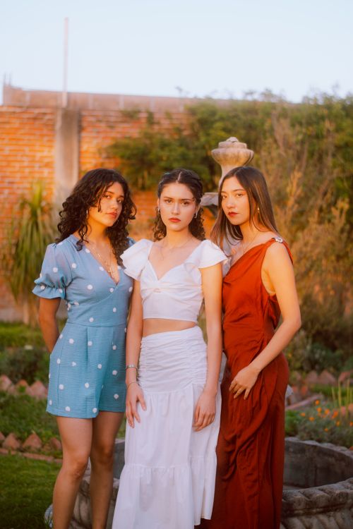 Free Three women in fashionable summer dresses pose outdoors at sunset. Stock Photo