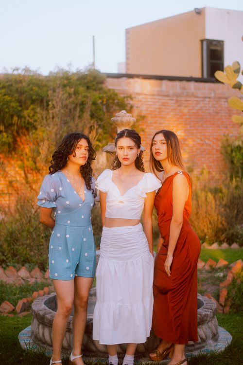 Free Three women standing by a fountain in an outdoor garden during sunset. Stock Photo