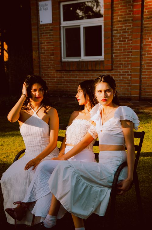 Free Three women in white dresses sitting on a bench, enjoying sunny weather. Stock Photo