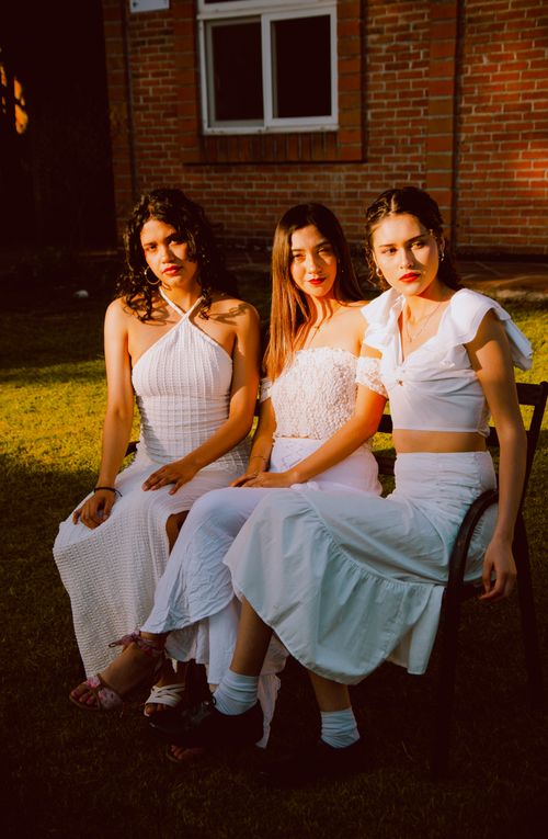 Free Three women in white dresses sitting outdoors in sunset lighting. Stock Photo