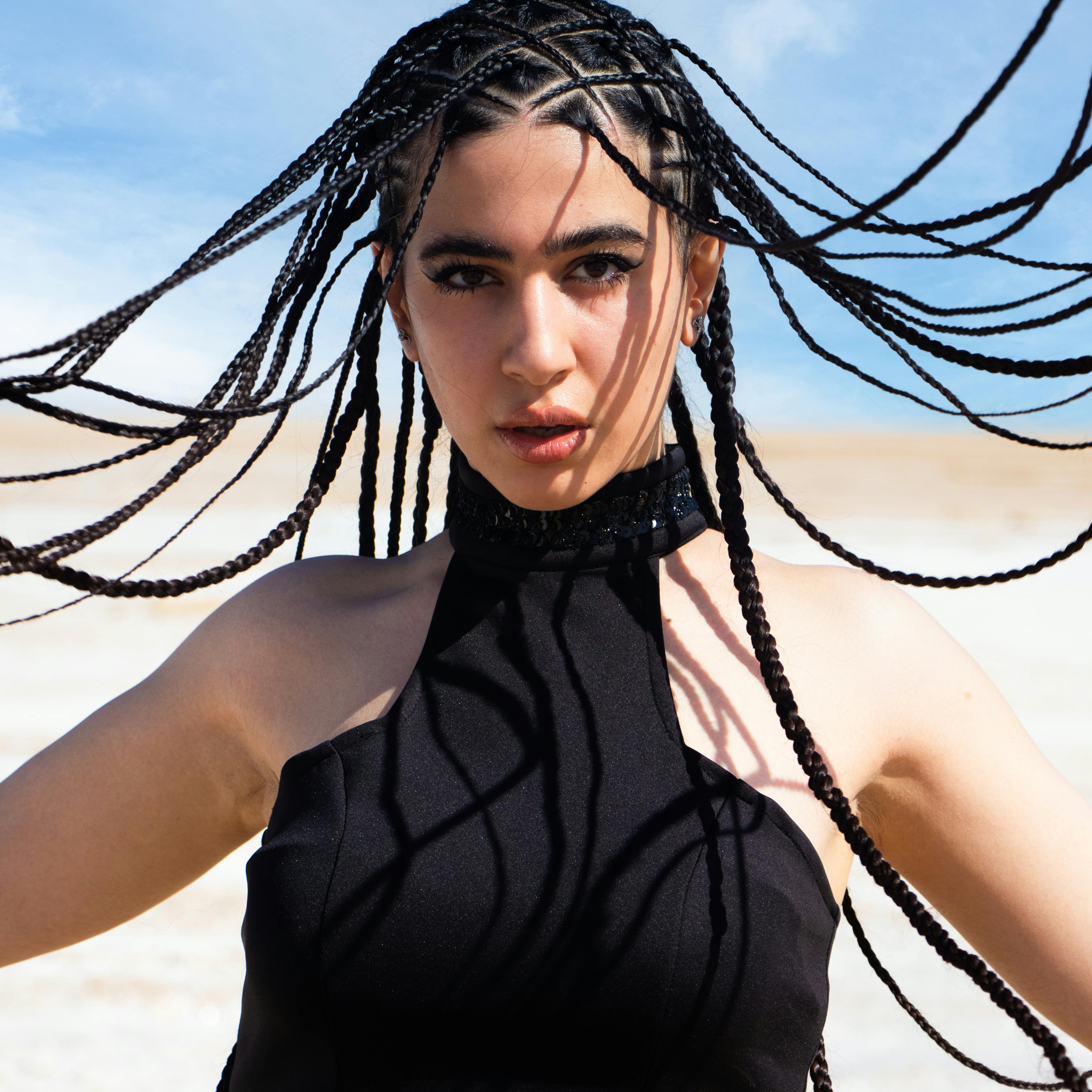 Gratis Retrato dinámico al aire libre de una mujer con cabello trenzado en una pose sorprendente bajo un cielo soleado. Foto de stock
