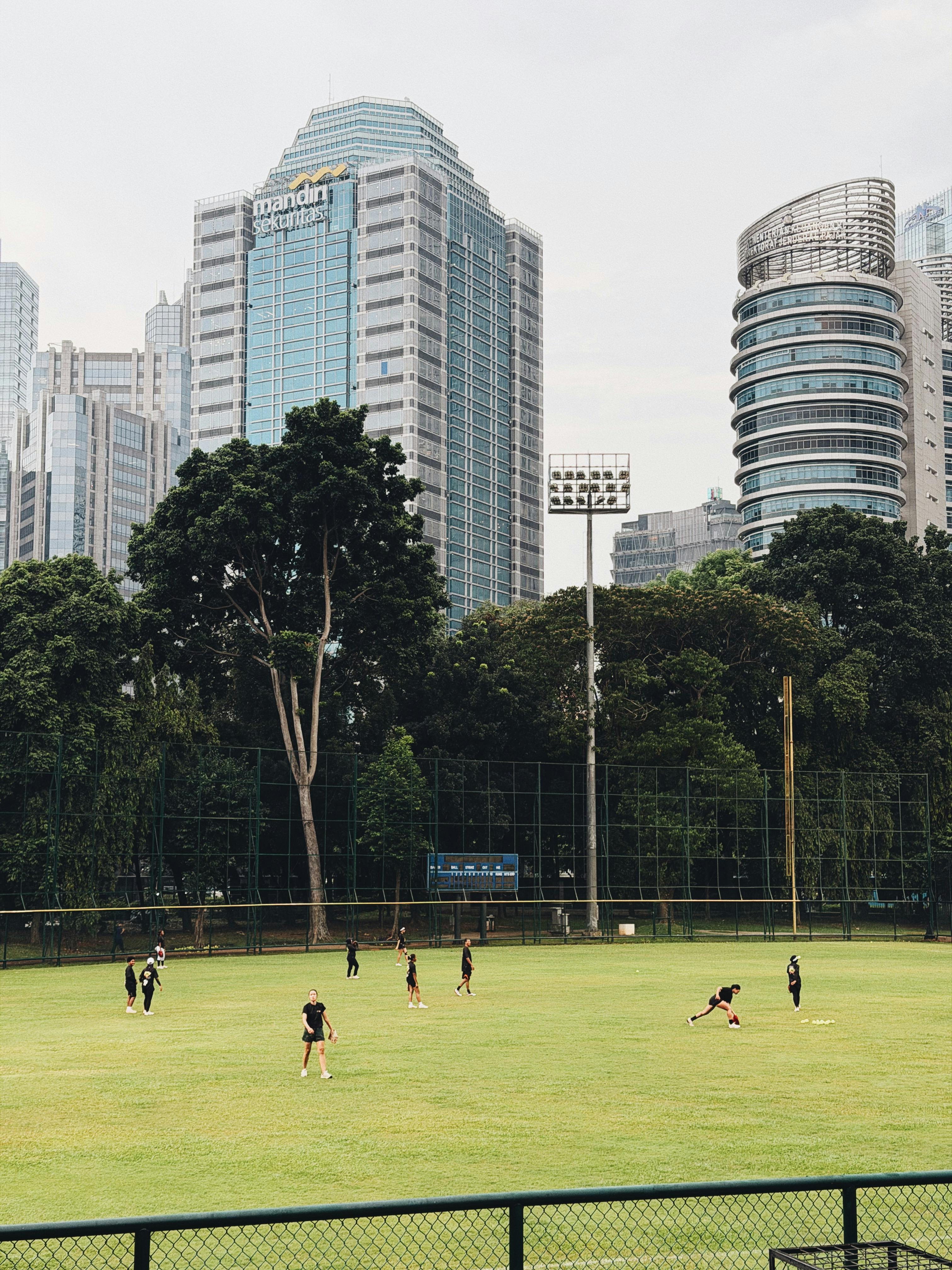 Youth playing soccer in a green field amid Jakarta's towering skyline.