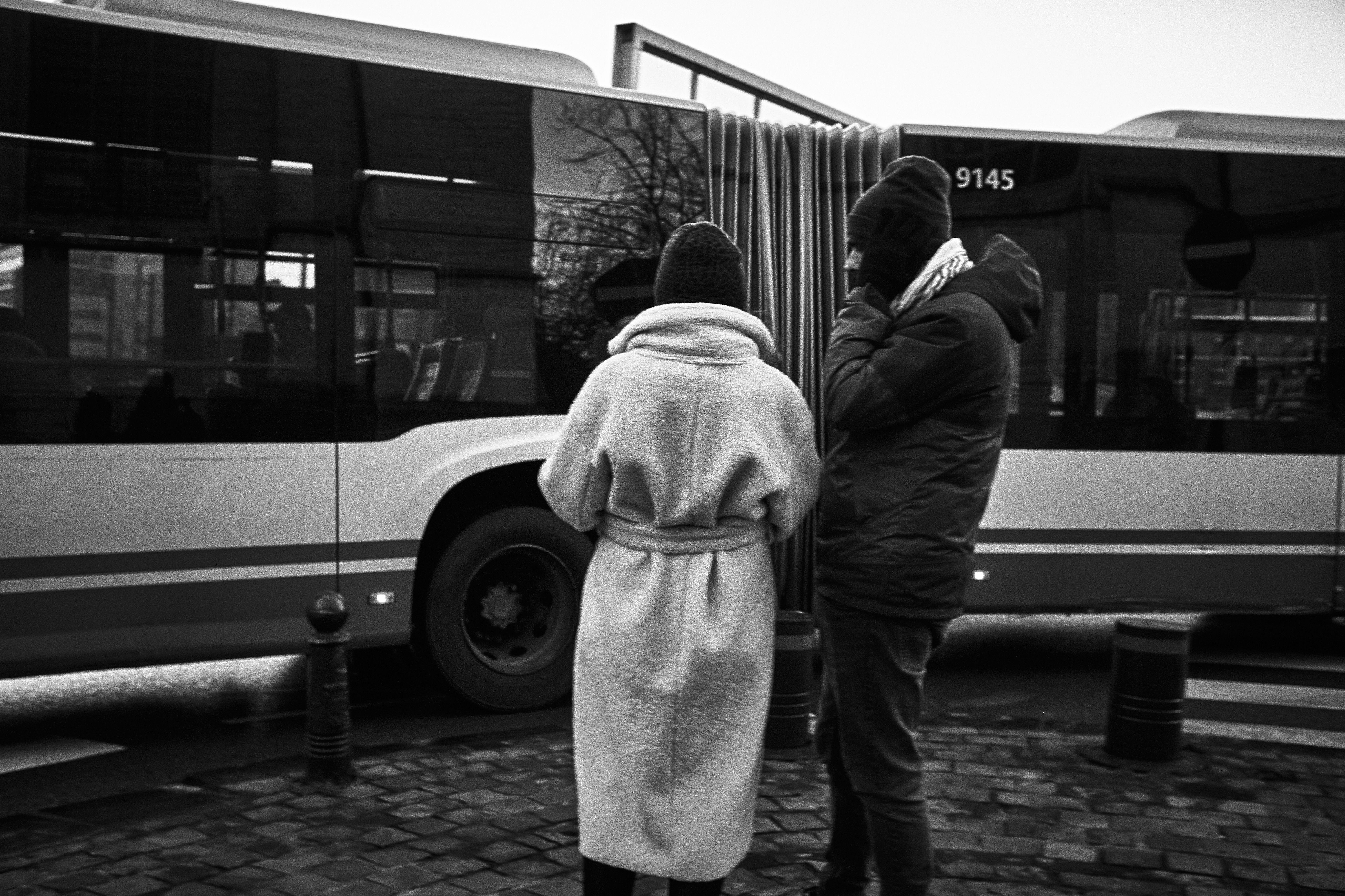 A couple in winter clothing standing at a bus stop in Brussels, Belgium.