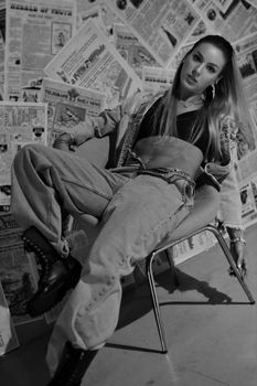 Stylish woman posing in denim with a newspaper collage backdrop. Edgy and modern.
