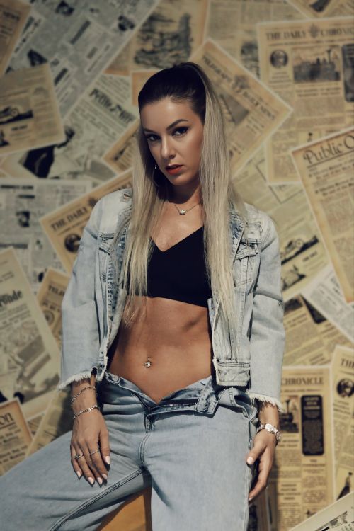 Free Stylish woman in denim attire posing against a backdrop of vintage newspapers, showcasing modern fashion trends. Stock Photo